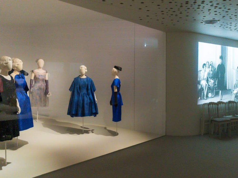 Vista lateral a parte de la exposición. Trajes de Balenciaga son expuestos y unas imágenes son proyectadas.