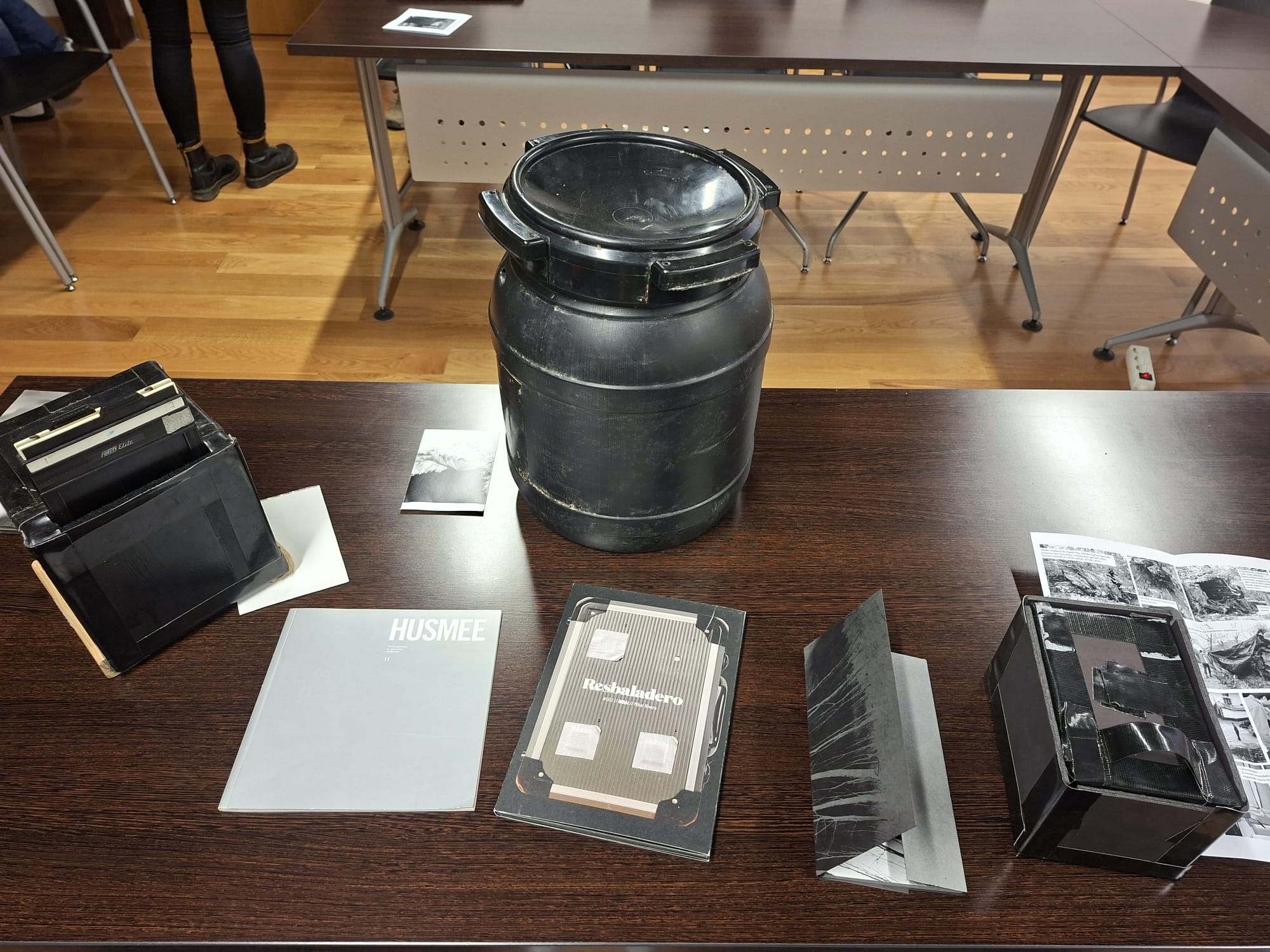 Mesa de exposición con varios recipientes y cajas negras utilizadas para sacar fotos.